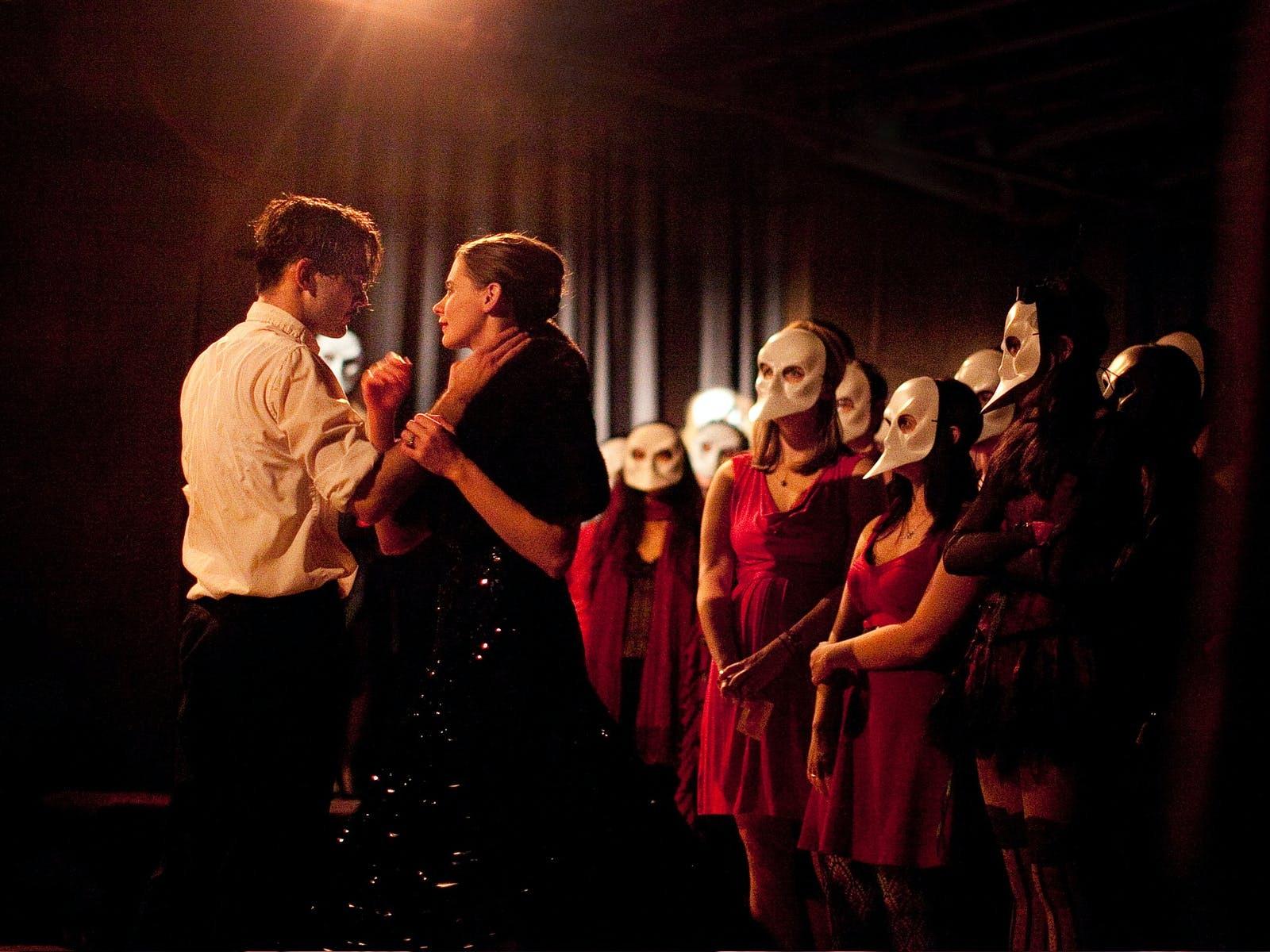 Masked audience members surrounding performers during Punchdrunk's Sleep No More at the McKittrick Hotel in New York
